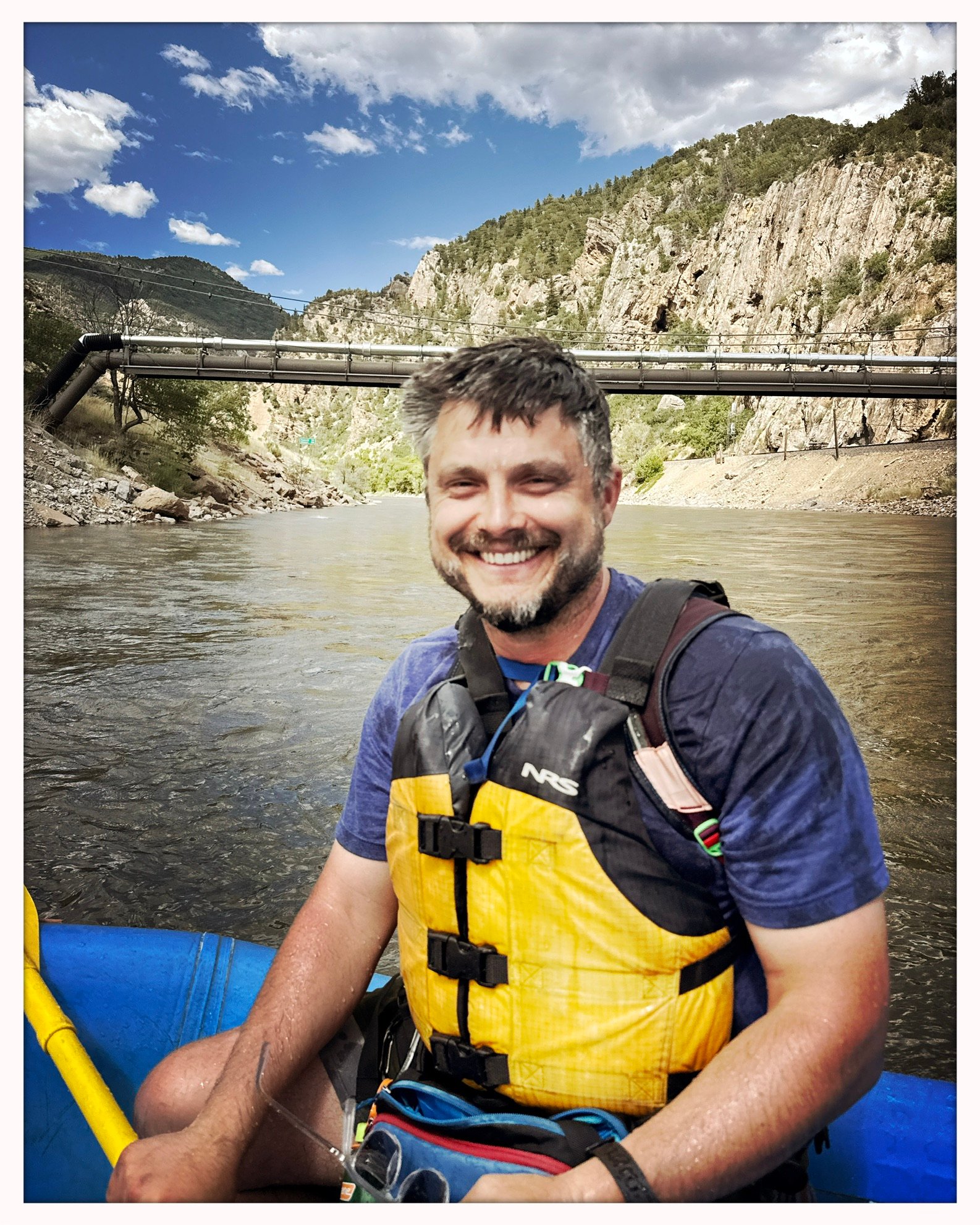 Nathan smiling in a raft on a river, wearing a life jacket