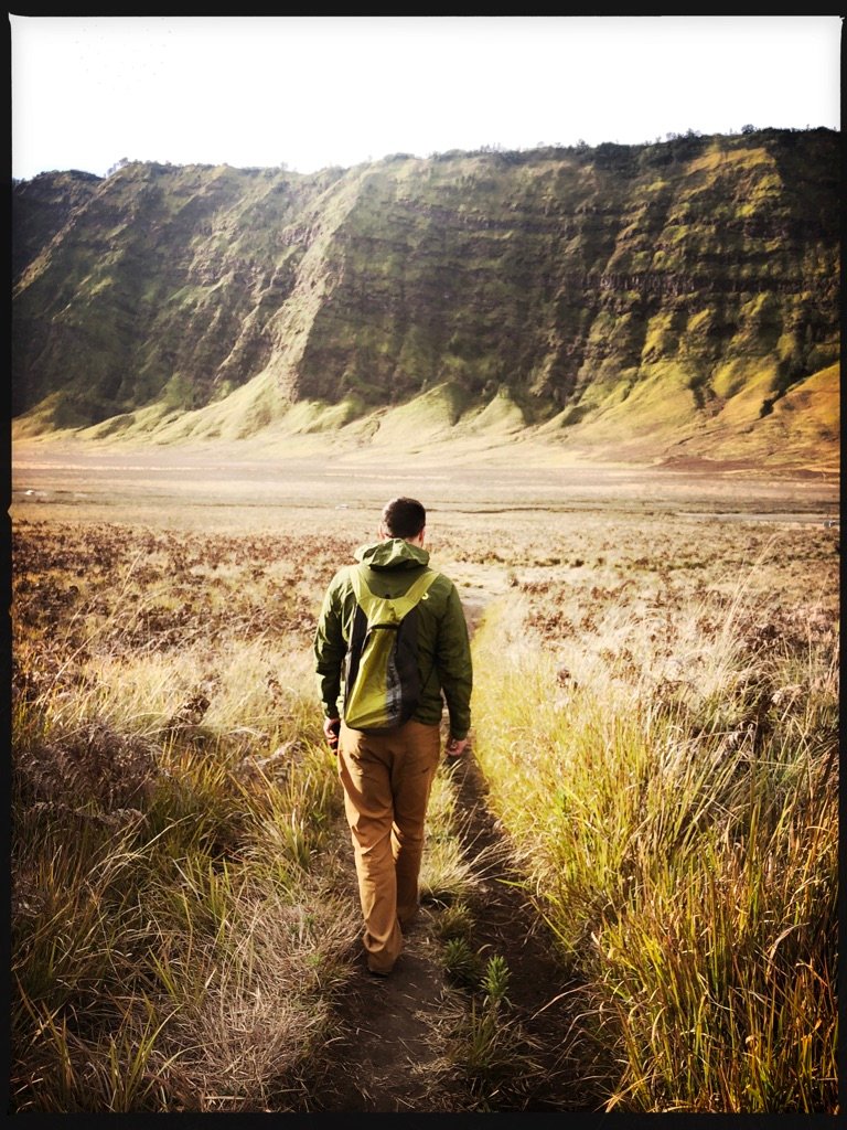 Nathan walking along a grassy path toward a steep green ridge